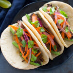 Three Korean beef tacos on a black plate.