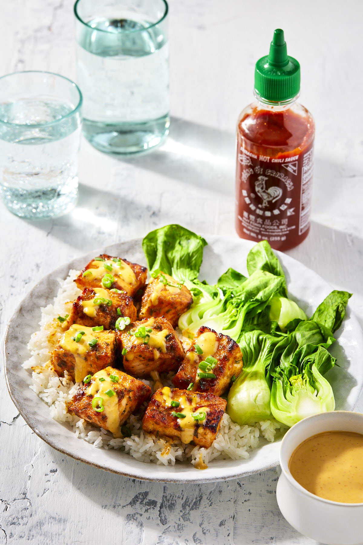 Honey sriracha salmon served with rice and bok choy on a white plate.
