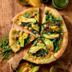 Slices of squash blossom pizza on a wooden board.