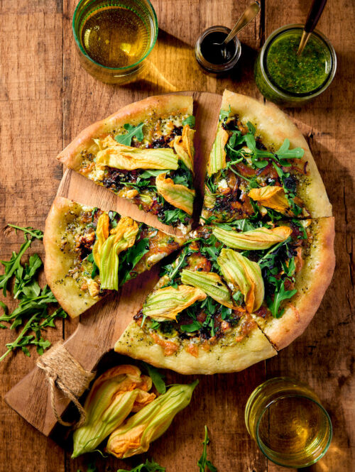 Slices of squash blossom pizza on a wooden board.