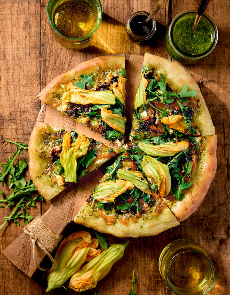 Slices of squash blossom pizza on a wooden board.
