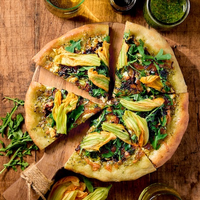 Slices of squash blossom pizza on a wooden board.