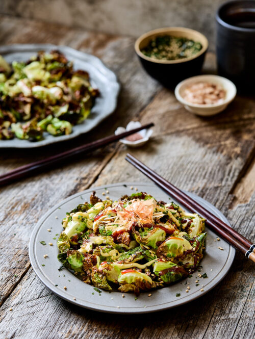 Twos plates of fried Brussels sprouts next to some chopsticks.