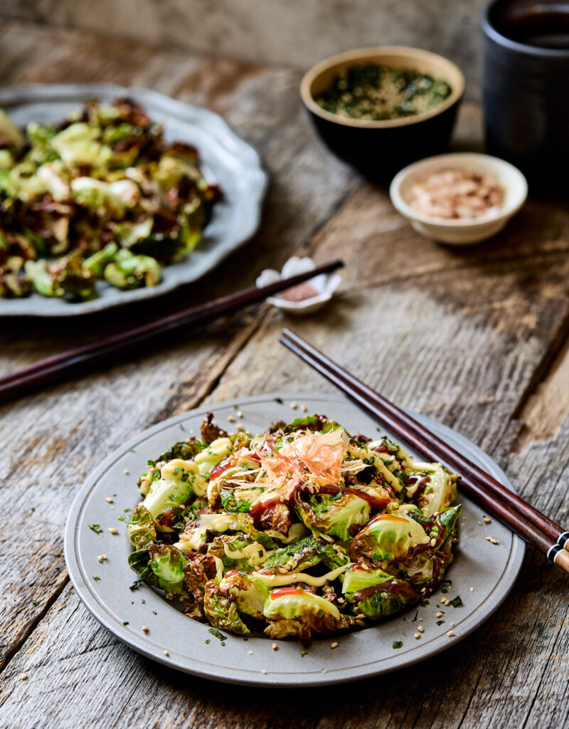 Twos plates of fried Brussels sprouts next to some chopsticks.