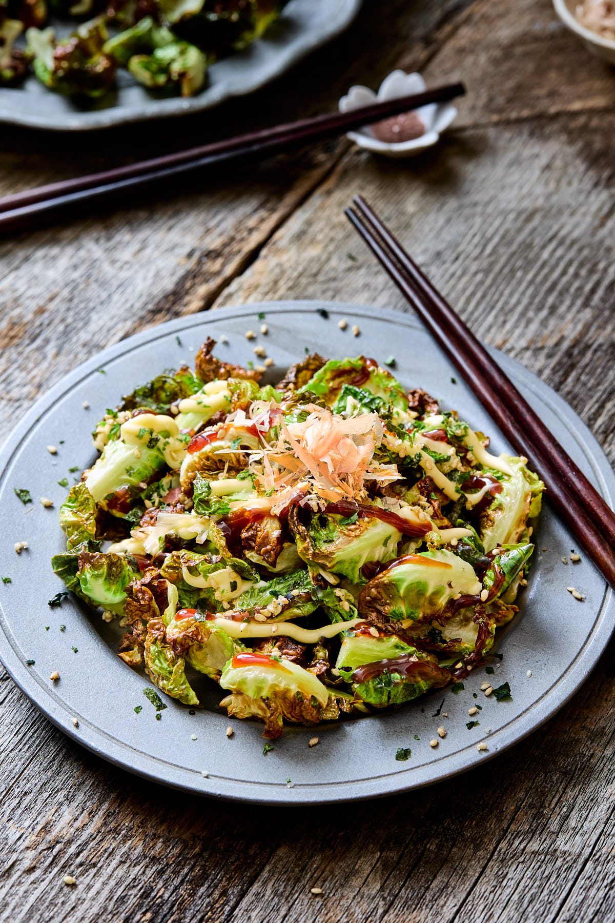 Plate of fried Brussels sprouts topped with katsu sauce, mayo, furikake, and bonito flakes.