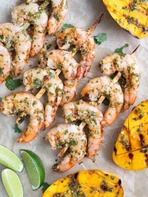 Skewers of grilled shrimp and grilled mango halves on parchment paper.