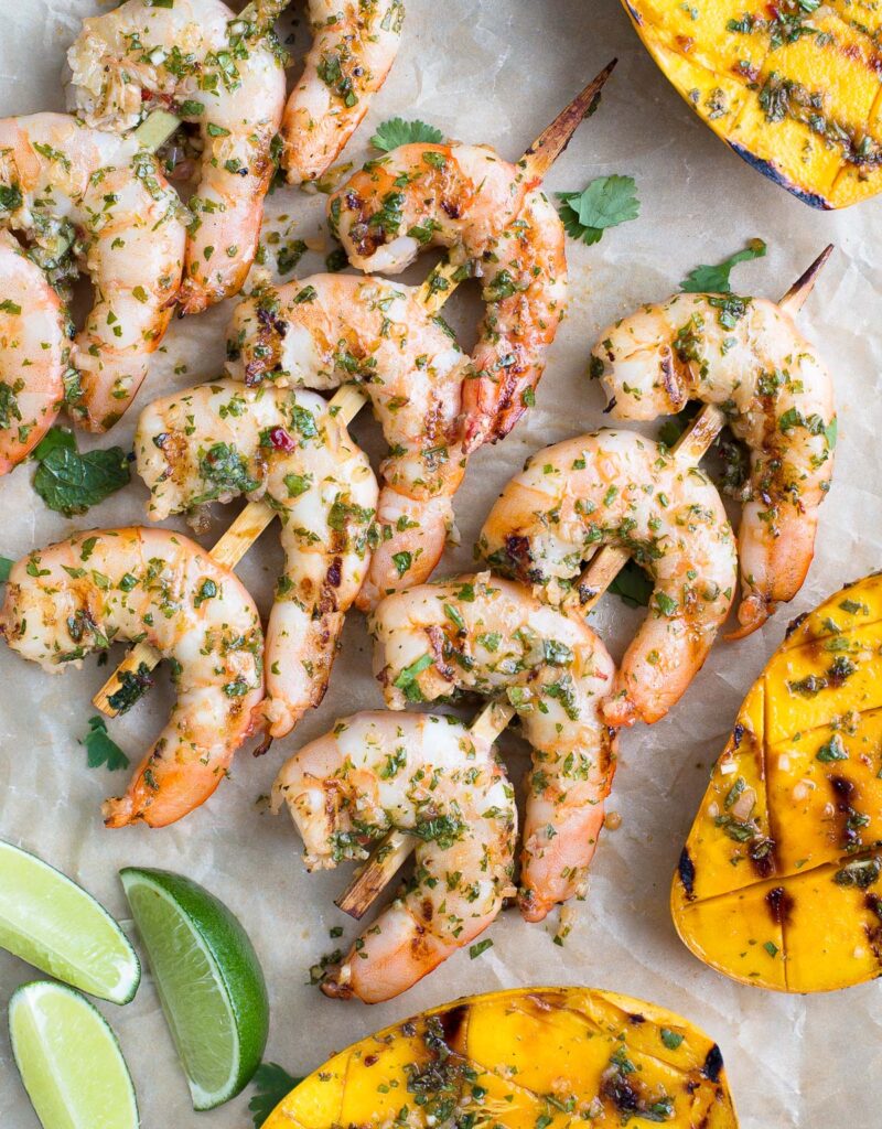 Skewers of grilled shrimp and grilled mango halves on parchment paper.