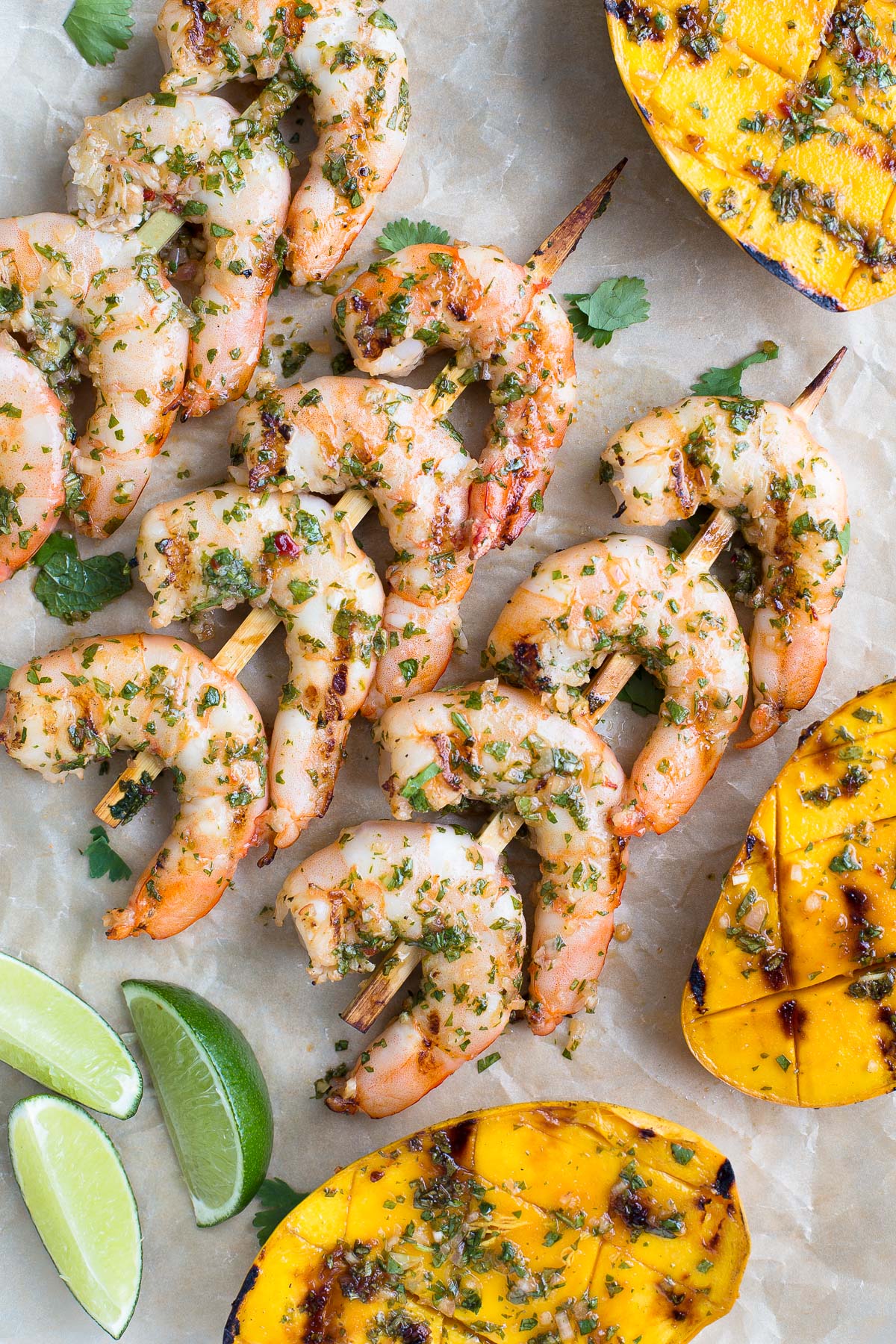 Skewers of grilled shrimp and grilled mango halves on parchment paper.