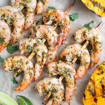 Skewers of grilled shrimp and grilled mango halves on parchment paper.