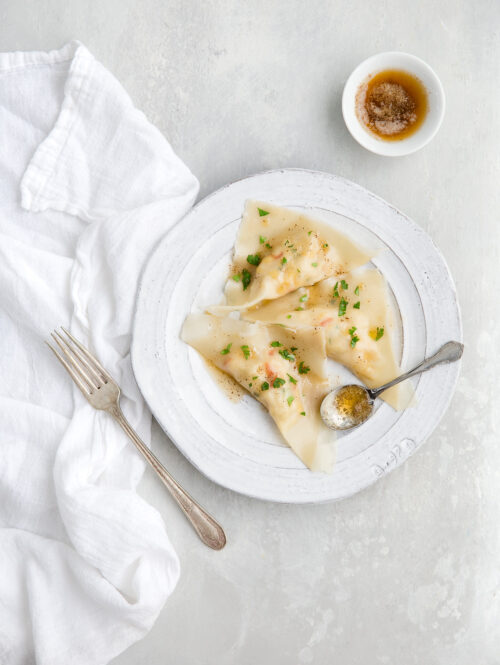 Some crab ravioli drizzled with browned butter on a white plate.
