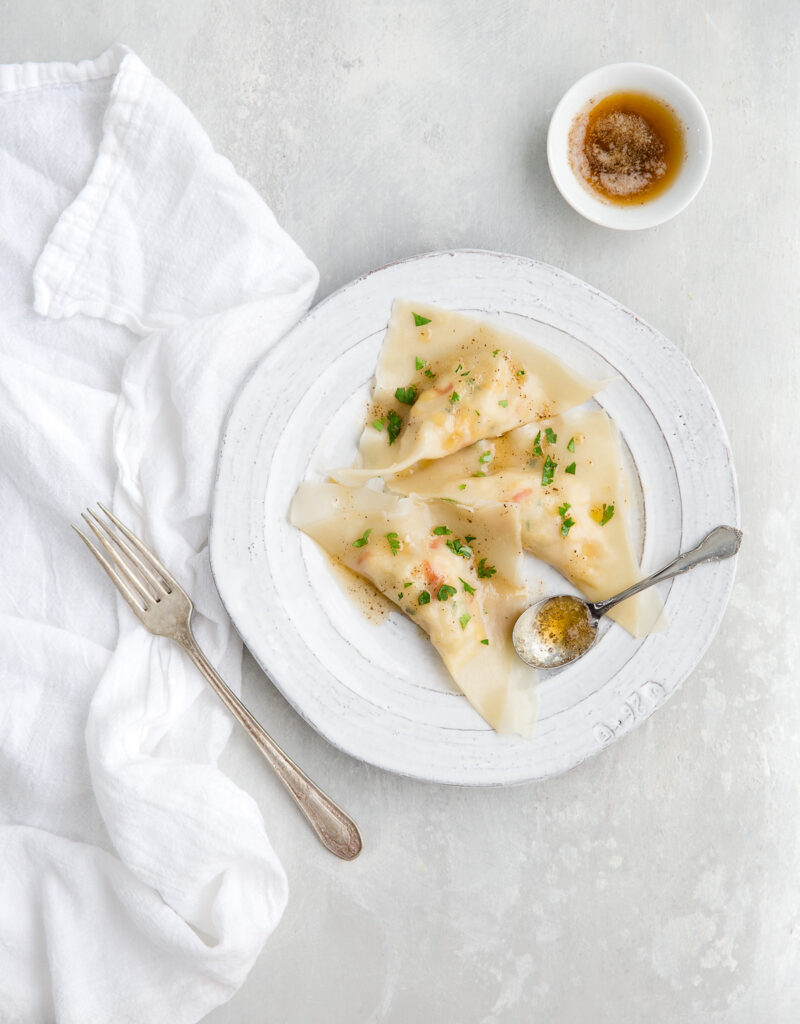 Some crab ravioli drizzled with browned butter on a white plate.