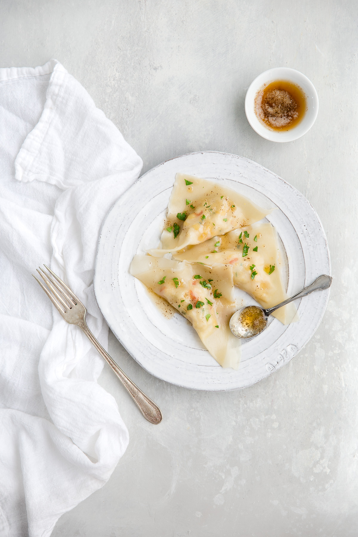 Some crab ravioli drizzled with browned butter on a white plate.