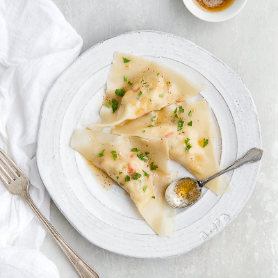 Some crab ravioli drizzled with browned butter on a white plate.