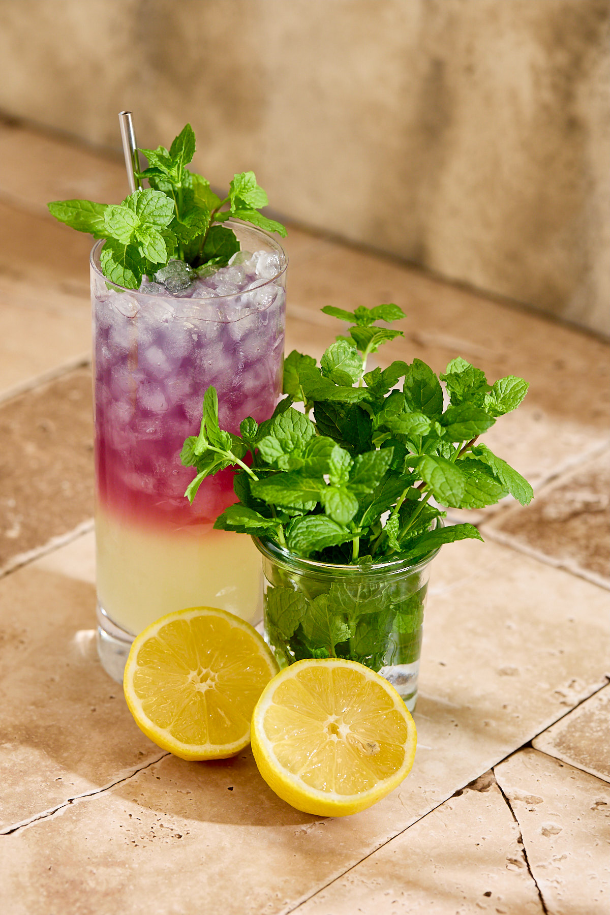 A glass of blackberry tea lemonade next lemon halves and mint sprigs.