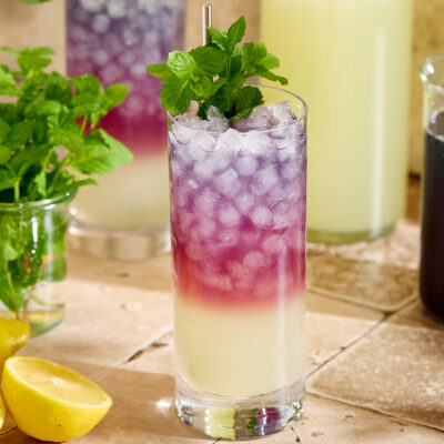 A glass of blackberry tea lemonade garnished with mint sprigs.