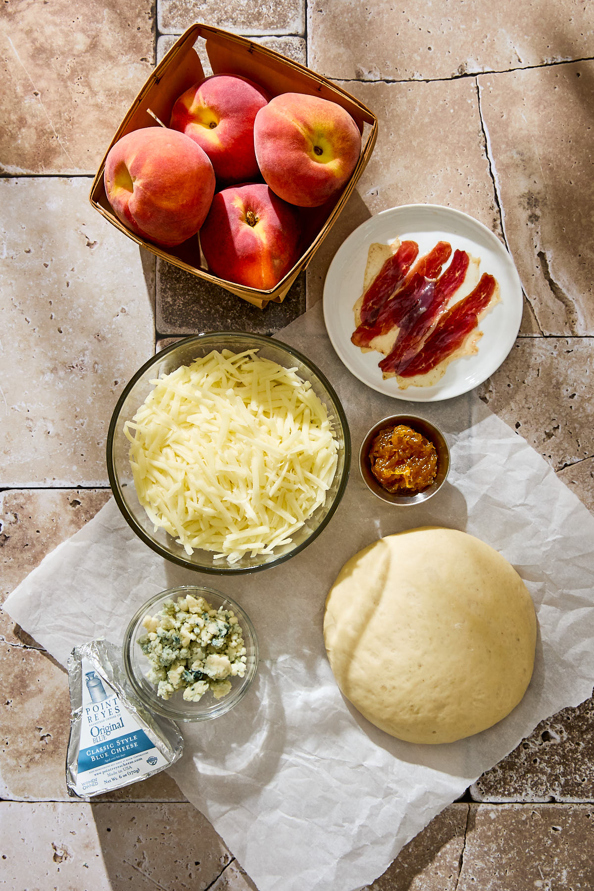 Ingredients for making peach pizza with duck prosciutto, and blue cheese on a stone background.