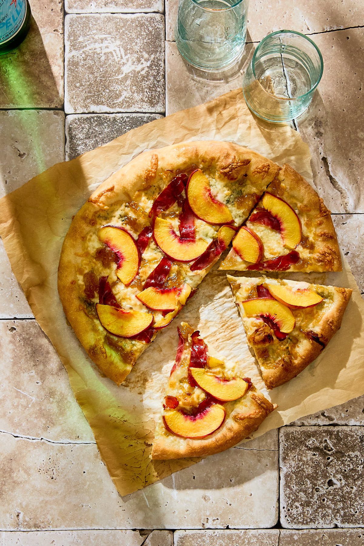 A peach and duck prosciutto pizza next to some glasses.