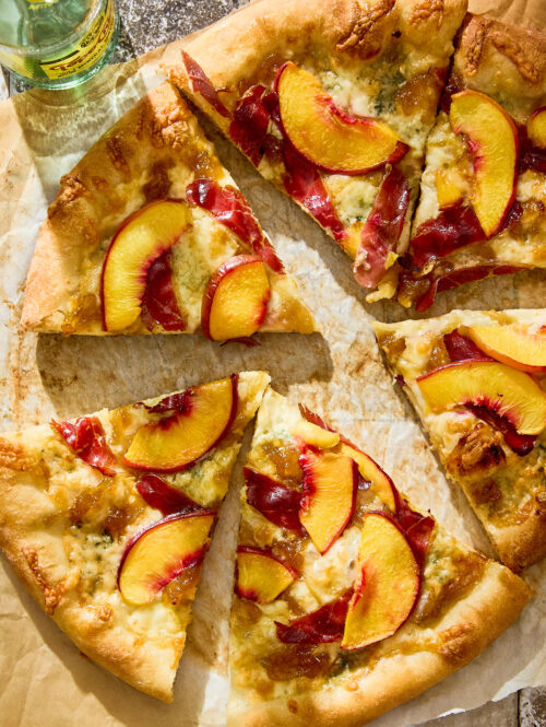 Slices of peach and duck prosciutto pizza on a piece of parchment paper.