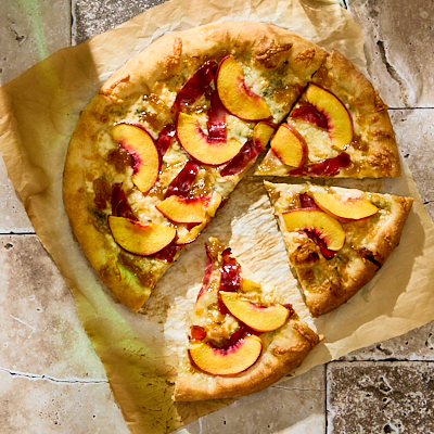 Slices of peach and duck prosciutto pizza on a piece of parchment paper.