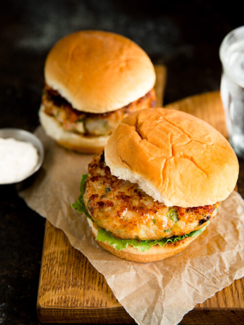 Two shrimp burgers on a piece of brown parchment paper on a small wooden board.