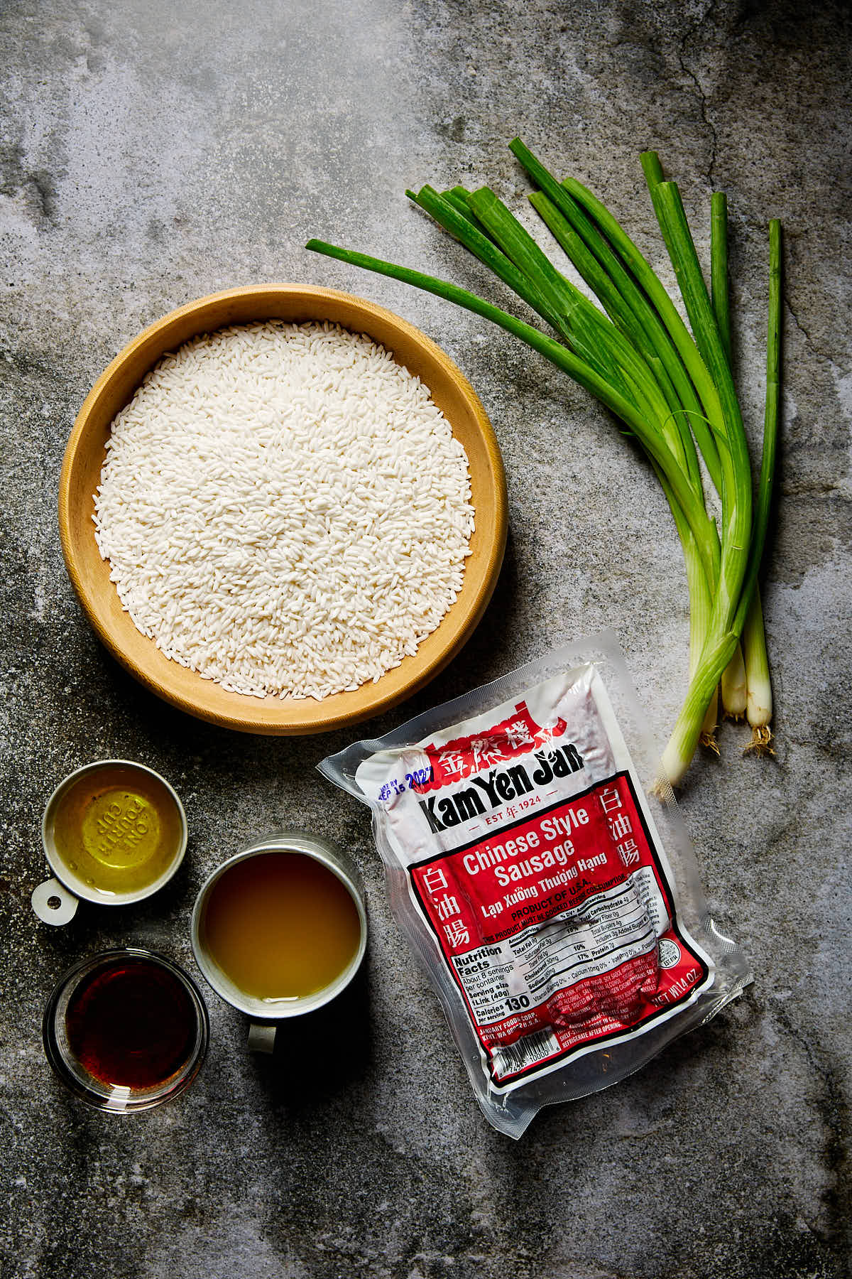 Ingredients for making sticky rice with Chinese sausage set out on a stone backdrop.