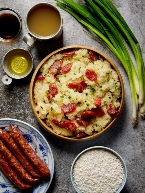 A plate of cooked sticky rice with Chinese sausage next to some ingredients.