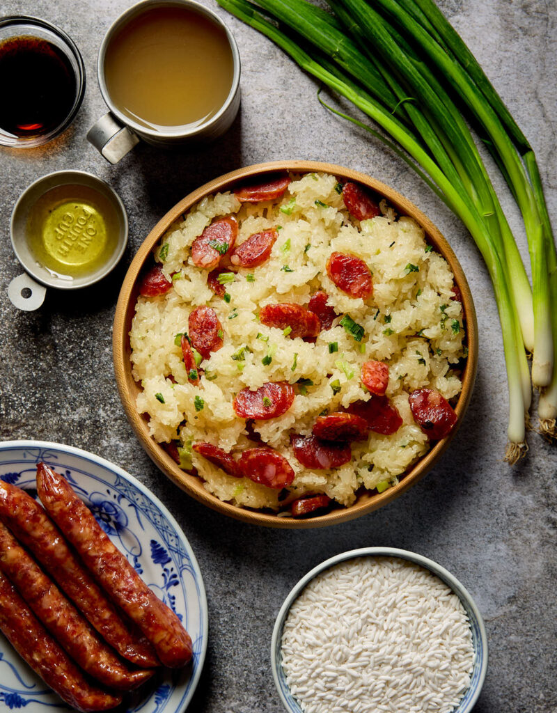 A plate of cooked sticky rice with Chinese sausage next to some ingredients.