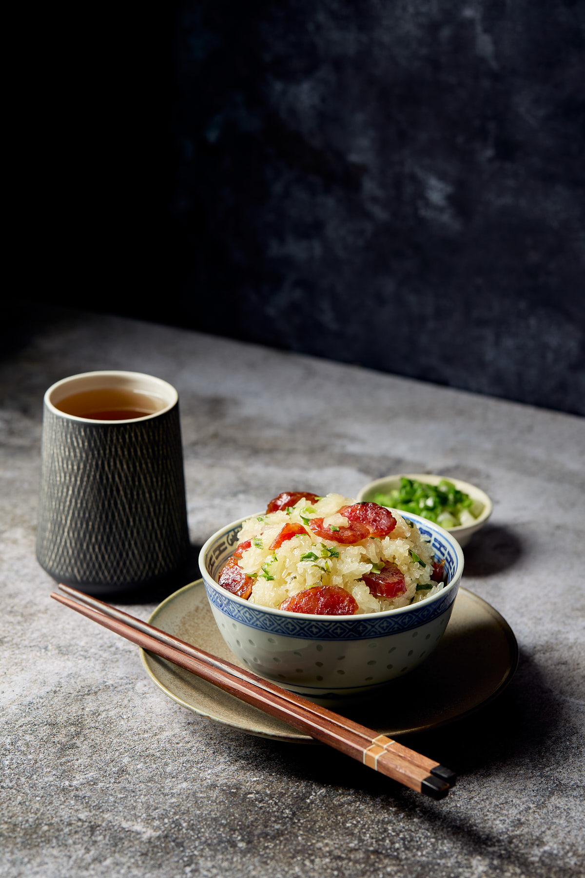A bowl of sticky rice with Chinese sausage next to a pair of chopsticks.